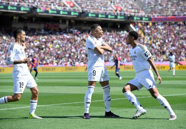 Real Madrid's French forward #09 Kylian Mbappe (C) celebrates with Real Madrid's English midfielder #05 Jude Bellingham after converting a penalty to score their first goal during the Spanish league football match between FC Barcelona and Real Madrid CF at Estadi Olimpic Lluis Companys in Barcelona, on May 11, 2025. (Photo by Josep LAGO / AFP)