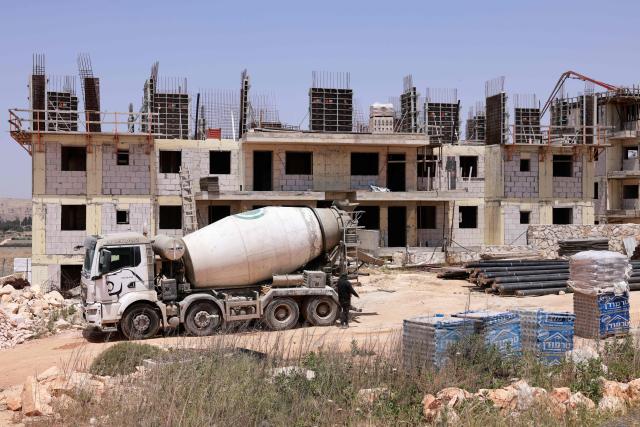 A worker walks next to a cement truck at a construction site for a housing project in the Israeli settlement of Har Brakha, south of Nablus in the occupied West Bank on May 11, 2025. (Photo by Menahem Kahana / AFP)