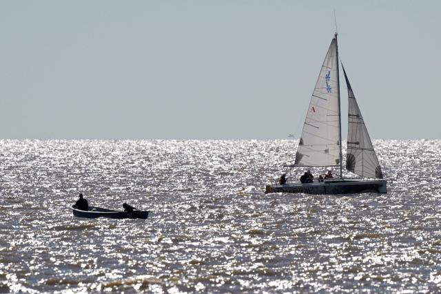 A sailboat sails alongside a boat fishing in the Rio de la Plata river in Buenos Aires on May 11, 2025. (Photo by JUAN MABROMATA / AFP)