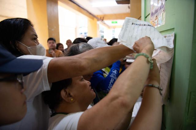 Voters jostle with one another as they look for their names in a registration list for the mid-term election at a polling station in Manila on May 12, 2025. Millions of Filipinos headed to the polls May 12 in a mid-term election widely seen as a referendum on the explosive feud between President Ferdinand Marcos and impeached Vice President Sara Duterte. (Photo by Ted ALJIBE / AFP)