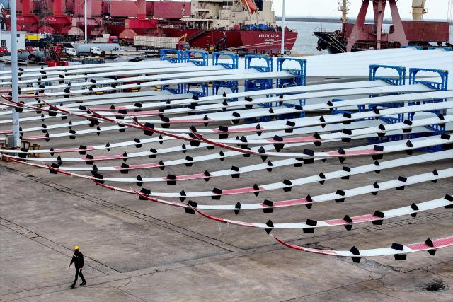 This photo taken on May 10, 2025 shows a worker walking past wind turbine blades for export at the port in Lianyungang, in China’s eastern Jiangsu province. (Photo by AFP) / China OUT