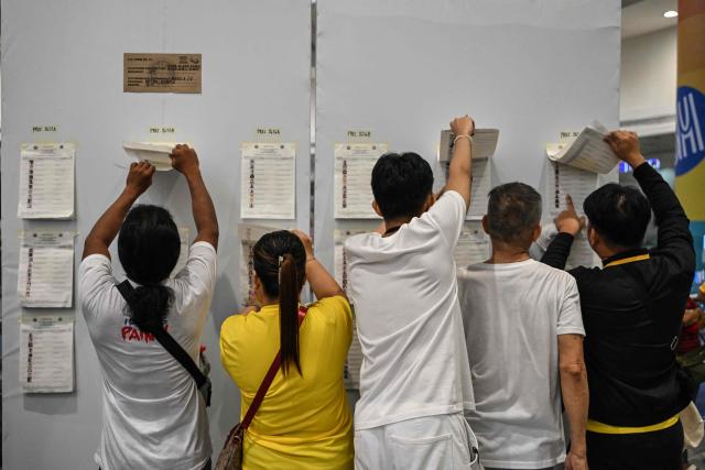Voters look for their names in a registration list for the mid-term election at a polling station set up in a mall in Manila on May 12, 2025. Millions of Filipinos headed to the polls May 12 in a mid-term election widely seen as a referendum on the explosive feud between President Ferdinand Marcos and impeached Vice President Sara Duterte. (Photo by Jam STA ROSA / AFP)