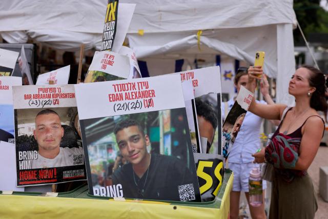 A woman takes pictures of posters bearing portraits of Israeli hostages held by Hamas in Gaza since October 2023, including one with the face of Israeli-US captive Edan Alexander (C), at Hostages Square in Tel Aviv on May 12, 2025. Palestinian militant group Hamas announced on May 11, 2025 it would release Alexander as part of talks with the United States towards a ceasefire. (Photo by Menahem KAHANA / AFP)