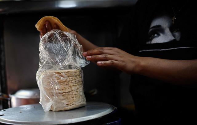 A worker handles a tortilla at a street food stall in the Roma neighborhood in Mexico City on May 8, 2025. Peering through a microscope, food scientist Raquel Gomez studies microorganisms that add nutrients and help to preserve tortillas for longer without refrigerators that are a luxury in impoverished Mexican communities. (Photo by Alfredo ESTRELLA / AFP)