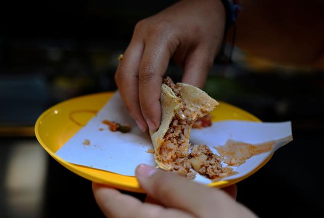 A woman eats a taco at a street food stall in the Roma neighborhood in Mexico City in May 8, 2025. Peering through a microscope, food scientist Raquel Gomez studies microorganisms that add nutrients and help to preserve tortillas for longer without refrigerators that are a luxury in impoverished Mexican communities. (Photo by Alfredo ESTRELLA / AFP)