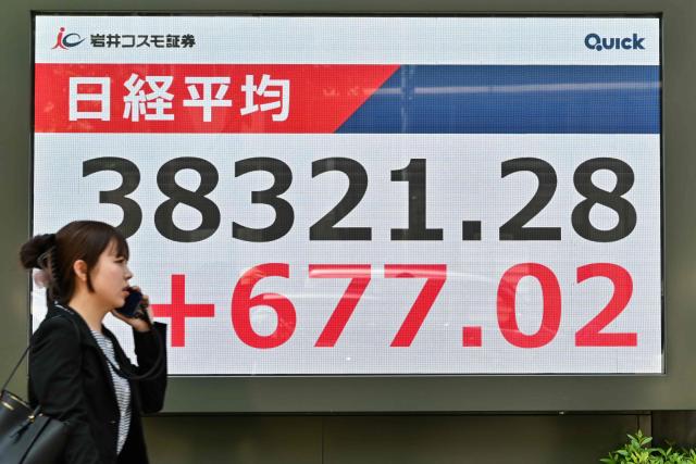 A pedestrian walks past an electronic board showing share prices during morning trading on the Tokyo Stock Exchange along a street in central Tokyo on May 13, 2025. (Photo by Richard A. Brooks / AFP)