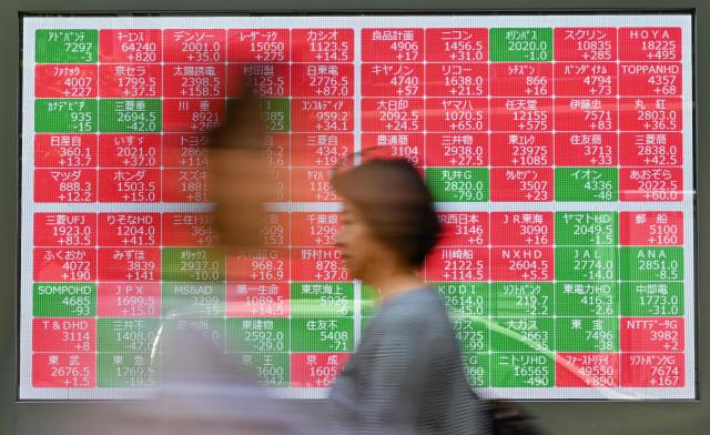 Pedestrians walk past an electronic board showing share prices during morning trading on the Tokyo Stock Exchange along a street in central Tokyo on May 13, 2025. (Photo by Richard A. Brooks / AFP)