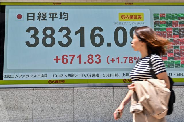 A pedestrian walks past an electronic board showing share prices during morning trading on the Tokyo Stock Exchange along a street in central Tokyo on May 13, 2025. (Photo by Richard A. Brooks / AFP)