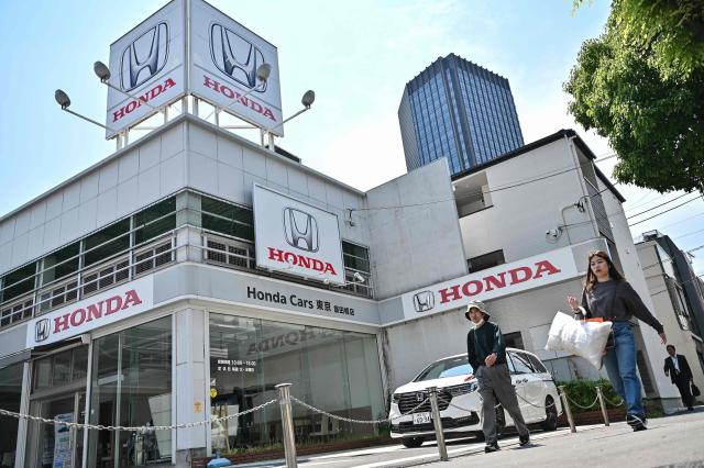 Pedestrians walk past a car dealership for Japanese automaker Honda Motor along a street in central Tokyo on May 13, 2025, ahead of the company's annual results announcement later in the day. (Photo by Richard A. Brooks / AFP)