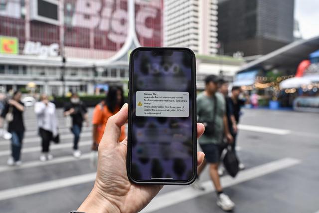 A message from Thailand's Department of Disaster Prevention and Mitigation (DDPM) is pictured on a smartphone during a test run for an emergency cell broadcast system in Bangkok on May 13, 2025. (Photo by Lillian SUWANRUMPHA / AFP)
