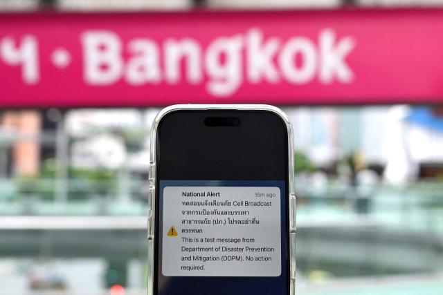 A message from Thailand's Department of Disaster Prevention and Mitigation (DDPM) is pictured on a smartphone during a test run for an emergency cell broadcast system in Bangkok on May 13, 2025. (Photo by Manan VATSYAYANA / AFP)