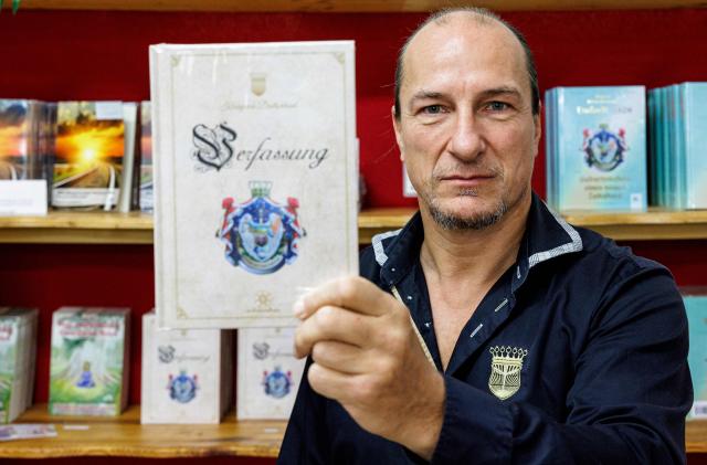 (FILES) In this file photo taken on October 23, 2023 Peter Fitzek, self-proclaimed head of the so-called 'Kingdom of Germany' (Koenigreich Deutschland), poses for a photo with the kingdom's constitution, in Wittenberg, eastern Germany. German authorities on May 13, 2025 launched multiple raids against an extremist network and dissolved the so-called "Kingdom of Germany", the interior ministry said. The Federal Prosecutor's Office also announced the arrest of four people during the raids, including three founding members of the group. Described as "dangerous extremists" by the ministry, the Kingdom of Germany is part of the German conspiracy movement known as the "Citizens of the Reich", which rejects the legitimacy of the modern German republic. (Photo by JENS SCHLUETER / AFP)