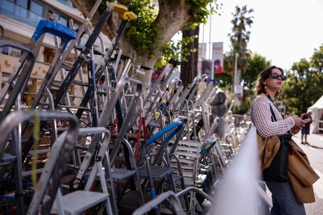 An attendee rests against an enclosure where fans and photographers have set up step-ladders across the street from the red carpet, on the Boulevard de la Croisette, on the opening day of the 78th edition of the Cannes Film Festival in Cannes, southern France, on May 13, 2025. (Photo by Ian LANGSDON / AFP)