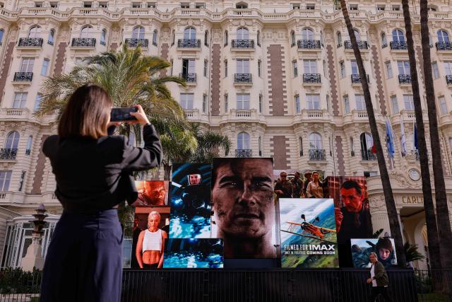 A woman takes a photograph of giant screen promoting the film "Mission: Impossible – The Final Reckoning" starring US actor Tom Cruise in front of the Carlton hotel, on the Boulevard de la Croisette, on the opening day of the 78th edition of the Cannes Film Festival in Cannes, southern France, on May 13, 2025. (Photo by Ian LANGSDON / AFP)