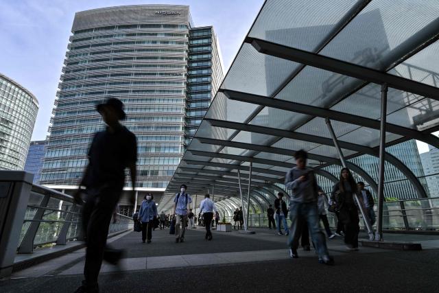 Pedestrians walk along an elevated passageway outside the headquarters building (back C) for Japanese automaker Nissan in the city of Yokohama, Kanagawa prefecture on May 13, 2025. Japanese automaker Nissan posted a huge annual net loss of 4.5 billion USD on May 13, while confirming reports that it planned to cut 20,000 jobs worldwide. (Photo by Richard A. Brooks / AFP)