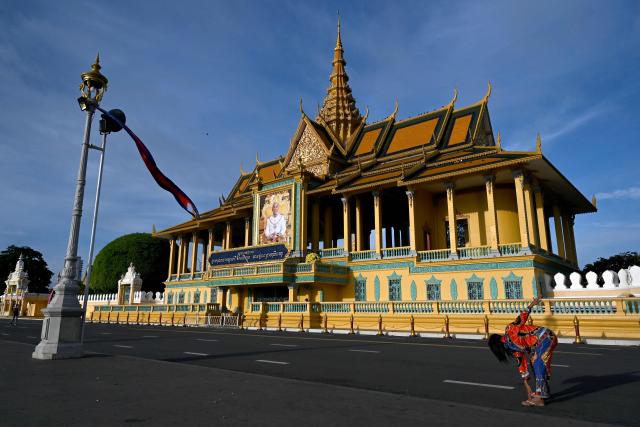 A woman exercises near a portrait of King Norodom Sihamoni in front of the Royal Palace in Phnom Penh on May 14, 2025. Cambodia is celebrating King Norodom Sihamoni's 72nd birthday with events to be held on May 13-15. (Photo by TANG CHHIN Sothy / AFP)