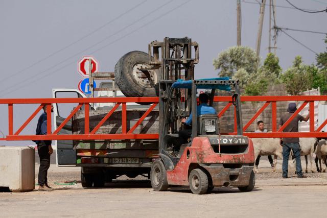 A fork lift places a tire on a truck over an metal gate set up by the Israeli army in Qusra, in the occupied West Bank, on May 12, 2025. Israel heavily restricts the movement of West Bank Palestinians, who must obtain permits from authorities to travel through checkpoints and cross into east Jerusalem or Israel. (Photo by Jaafar ASHTIYEH / AFP)