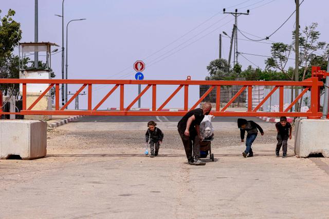 A Palestinian man and children cross an metal gate set up by the Israeli army in Qusra, in the occupied West Bank, on May 12, 2025. Israel heavily restricts the movement of West Bank Palestinians, who must obtain permits from authorities to travel through checkpoints and cross into east Jerusalem or Israel. (Photo by Jaafar ASHTIYEH / AFP)