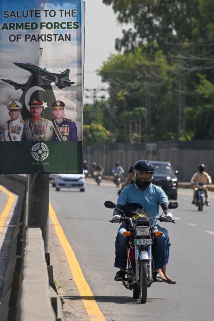 Commuters ride past a poster featuring Pakistan's Army Chief General Syed Asim Munir (C), Naval Chief Admiral Naveed Ashraf (L) and Air Chief Marshal Zaheer Ahmed Babar Sidhu (R) along a street in Rawalpindi on May 14, 2025. The brief conflict between India and Pakistan last week may have left no clear victor, but Islamabad's generals are taking a win, riding a wave of approval on social media to burnish their recently tarnished image. (Photo by Farooq NAEEM / AFP)