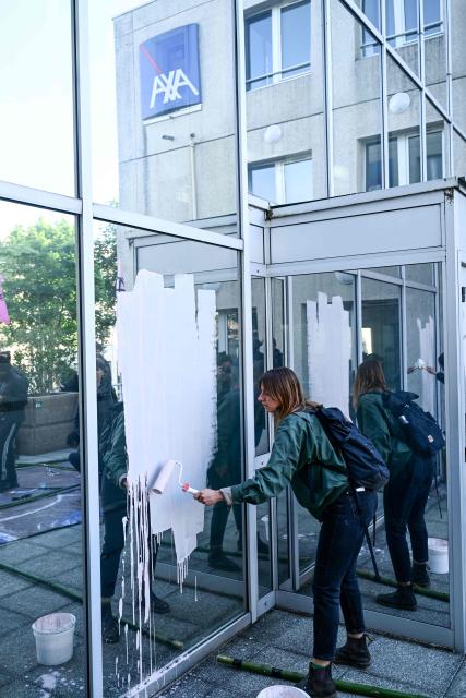 A climate activist from the Extinction Rebellion (XR) group paints the facade of the local headquarters of French insurance company AXA which they blame for financing fossil fuels and investing in the TotalEnergies group, in Nantes, western France, on May 14, 2025. (Photo by Sebastien Salom-Gomis / AFP)
