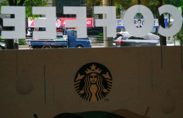 Banners showing South Korea's presidential election candidates, frontrunner Lee Jae-myung (top R), and main conservative rival Kim Moon-soo (top L), are seen beyond signage of coffee giant Starbucks in Seoul on May 15, 2025. Starbucks in South Korea has banned customers from using the names of the country's presidential candidates -- or the disgraced ex-president -- for their orders, the coffee giant told AFP on May 14. (Photo by ANTHONY WALLACE / AFP)