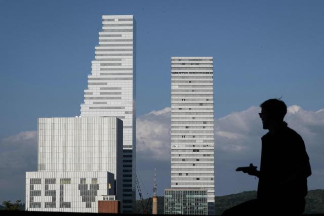 A man holds a cell phone as he stands facing the giant pharmaceutical Roche Towers with an ESC (Eurovision Song Contest -Love) sign created by blinded windows, in Basel on May 15, 2025. (Photo by SEBASTIEN BOZON / AFP)