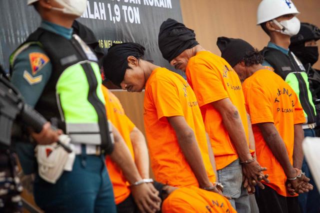 One Thai and four Myanmar suspects stand during a press conference with 705 kg of methamphetamine and 1.2 tonnes of cocaine seized from a Thai fishing boat, at a naval base in Batam, Riau Islands on May 17, 2025. (Photo by Andaru AK / AFP)