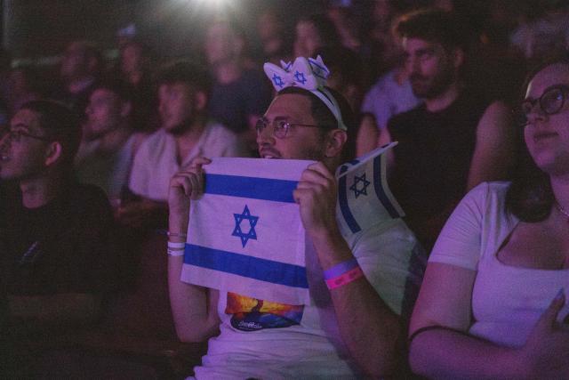 A man holds an Israeli flag as people watch the 2025 Eurovision Song Contest finals being screened at a community center in Tel Aviv, Israel, early on May 18, 2025. Austria's JJ won the 2025 Eurovision Song Contest on May 18, with his operatic song "Wasted Love" triumphing at the world's biggest live music television event. After the nail-biting drama as the votes were revealed running into Sunday morning, Austria finished with 436 points, ahead of Israel on 357 and Estonia on 356. (Photo by Maya Levin / AFP)