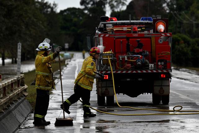 Fire Brigade officials clear silt as floodwaters recede from the main road in Taree on May 23, 2025. Record floods cut a destructive path through eastern Australia on May 23, caking houses in silt, washing out roads and separating 50,000 people from help. (Photo by Saeed KHAN / AFP)
