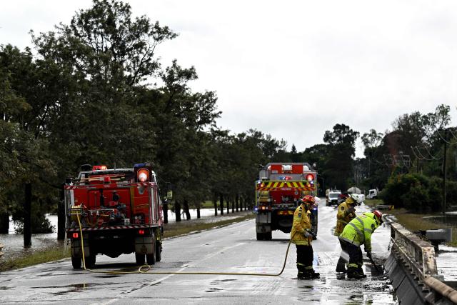 Fire Brigade officials clear silt as floodwaters recede from the main road in Taree on May 23, 2025. Record floods cut a destructive path through eastern Australia on May 23, caking houses in silt, washing out roads and separating 50,000 people from help. (Photo by Saeed KHAN / AFP)