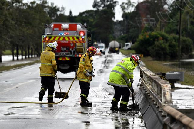 Fire Brigade officials clear silt as floodwaters recede from the main road in Taree on May 23, 2025. Record floods cut a destructive path through eastern Australia on May 23, caking houses in silt, washing out roads and separating 50,000 people from help. (Photo by Saeed KHAN / AFP)