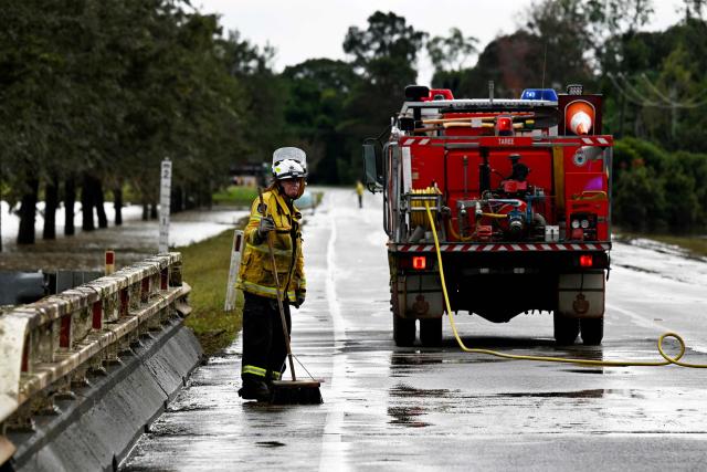 A Fire Brigade official clear silt as floodwaters recede from the main road in Taree on May 23, 2025. Record floods cut a destructive path through eastern Australia on May 23, caking houses in silt, washing out roads and separating 50,000 people from help. (Photo by Saeed KHAN / AFP)
