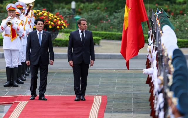 Vietnam's President Luong Cuong (L) and French President Emmanuel Macron inspect the honour guard during a welcome ceremony at the Presidential Palace in Hanoi on May 26, 2025. (Photo by Chalinee Thirasupa / POOL / AFP)