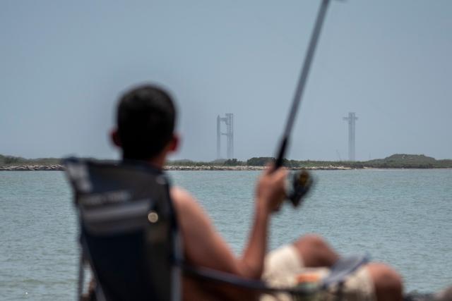 A man fishing looks at the SpaceX Starship rocket on the launchpad ahead of its scheduled launch from the SpaceX Starbase in Boca Chica as seen from South Padre Island, Texas on May 27, 2025. SpaceX said on My 23 it will make another launch attempt next week of the massive Starship rocket -- key to CEO Elon Musk's long-term vision of colonizing Mars -- after two consecutive in-flight explosions earlier this year. "The ninth flight test of Starship is preparing to launch as soon as Tuesday, May 27," the company said on its website, adding the launch window would open at 6:30 pm (2330 GMT) at its base in Texas. (Photo by Sergio FLORES / AFP)