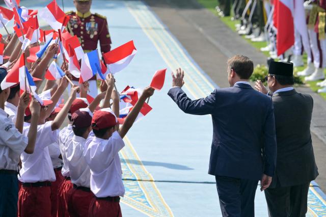 Indonesia's President Prabowo Subianto (R) and France's President Emmanuel Macron (2nd R) wave at children holding Indonesian and French national flags during a welcoming ceremony at Merdeka Palace in Jakarta on May 28, 2025. (Photo by BAY ISMOYO / AFP)