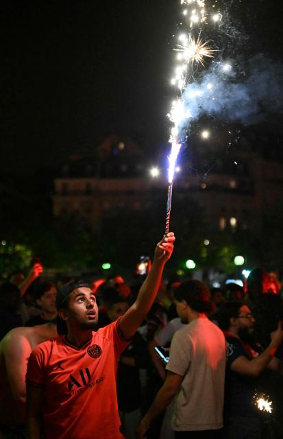 A Paris Saint-Germain (PSG) supporter holds a lit flare as he gathers with others on Place Trocadero as fireworks illuminate the word 'Champions' on The Eiffel Tower in Paris on May 31, 2025, during celebrations following their 5-0 victory in the UEFA Champions League final football match between Paris Saint-Germain (PSG) and Inter Milan held in Munich. (Photo by Hugo MATHY / AFP)