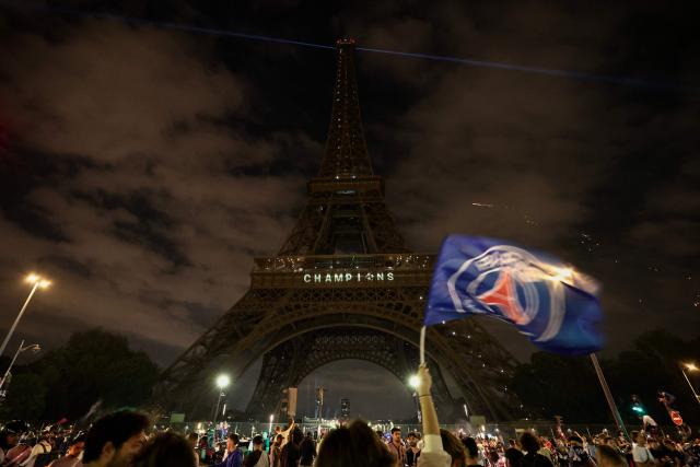 TOPSHOT - A Paris Saint-Germain's supporter holds a PSG flag in front of The Eiffel Tower reading "Champions" in Paris on May 31, 2025, during celebrations following their 5-0 victory in the UEFA Champions League final football match between Paris Saint-Germain (PSG) and Inter Milan held in Munich. (Photo by Thibaud MORITZ / AFP)