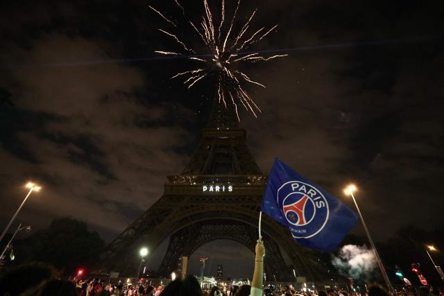 A Paris Saint-Germain's supporter holds a PSG flag as fireworks explode in front of The Eiffel Tower reading "Paris" in Paris on May 31, 2025, during celebrations following their 5-0 victory in the UEFA Champions League final football match between Paris Saint-Germain (PSG) and Inter Milan held in Munich. (Photo by Thibaud MORITZ / AFP)