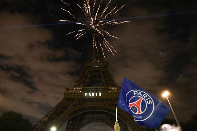 A Paris Saint-Germain's supporter holds a PSG flag as fireworks explode in front of The Eiffel Tower reading "Paris" in Paris on May 31, 2025, during celebrations following their 5-0 victory in the UEFA Champions League final football match between Paris Saint-Germain (PSG) and Inter Milan held in Munich. (Photo by Thibaud MORITZ / AFP)