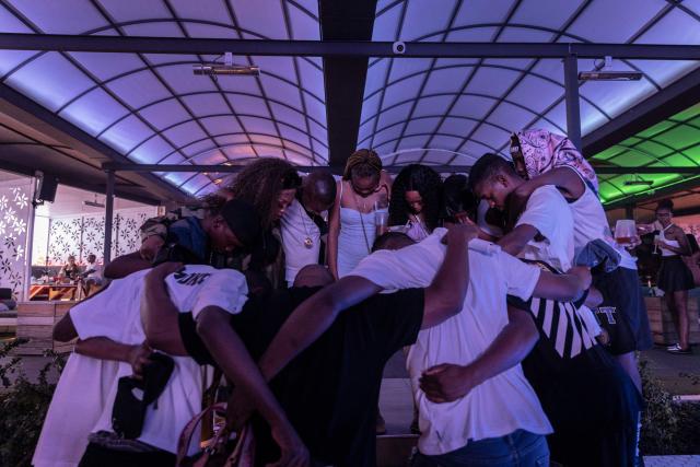 (FILES) South African amapiano dancer and singer Kamo Mphela (3L), Amapiano Artist of 2021, prays with her team before a performance at a nightclub in Johannesburg, on February 26, 2022. On a viral video of Manchester United’s Paul Pogba, fresh from a haircut, rhythmically jutting his chin to the sky to the catchy sound, or perhaps during a TikTok binge while trying to memorise a dancer’s slick footwork, you might have not known it then but that’s Amapiano -- a uniquely South African genre. “The pianos” in Zulu - what you hear blended in with some deep house, a jazzy soulful beat, and a lot of bass -  have catapulted from the country’s townships to the world. It’s "a whole culture movement, I don't wanna just say it's just a sound because it gets influenced by so many other stuff that are just part of the hood lifestyle,” Kamo Mphela, told AFP donning a sexy furry black-and-white outfit reminiscent of Disney’s Cruella de Vil. (Photo by GUILLEM SARTORIO / AFP)