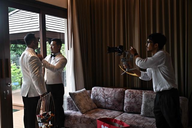Chinese nationals Song Jihan (2nd L) and Wang Zengyi (L) pose for a video shoot before their wedding ceremony near Pattaya in Chonburi province on May 31, 2025. When Wang Zengyi, 41, and Song Jihan, 29, first met at a friend's dinner party in China, it was love at first sight. Nearly three years later, the gay Chinese couple are getting married in Thailand, which became Asia's largest nation to legalise same-sex marriage earlier this year - including for foreign couples. (Photo by Lillian SUWANRUMPHA / AFP) / To go with Thailand-China-rights-LGBTQ, REPORTAGE by Sarah LAI (STF), Sally JENSEN
