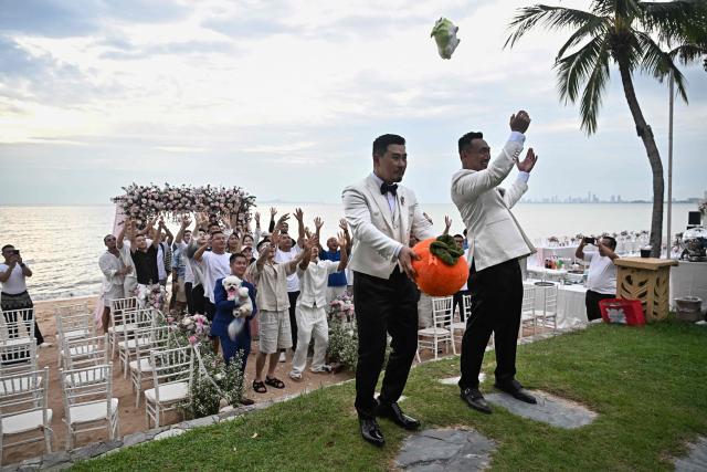 Chinese nationals Song Jihan (L) and Wang Zengyi (R) throw a plush cabbage and persimmon during their wedding ceremony near Pattaya in Chonburi province on May 31, 2025. When Wang Zengyi, 41, and Song Jihan, 29, first met at a friend's dinner party in China, it was love at first sight. Nearly three years later, the gay Chinese couple are getting married in Thailand, which became Asia's largest nation to legalise same-sex marriage earlier this year - including for foreign couples. (Photo by Lillian SUWANRUMPHA / AFP) / To go with Thailand-China-rights-LGBTQ, REPORTAGE by Sarah LAI (STF), Sally JENSEN