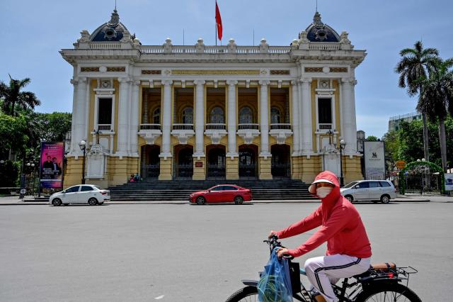 A woman wearing a long-sleeve top and a sun visor to protect against UV rays rides a bicycle past the Hanoi Opera House on a hot day in Hanoi on June 2, 2025. (Photo by Nhac NGUYEN / AFP)