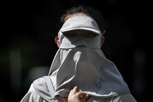 A woman wearing sun protective clothing walks on a hot day in Beijing on June 6, 2025. (Photo by WANG Zhao / AFP)