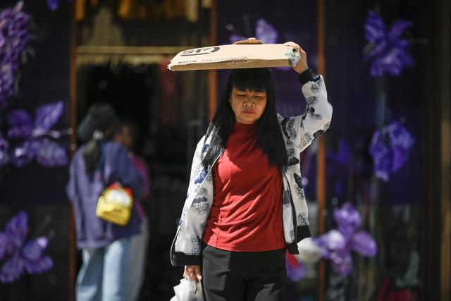 A woman uses a piece of cardboard to shelter from the sun while walking out of a buliding on a hot day in Beijing on June 6, 2025. (Photo by WANG Zhao / AFP)