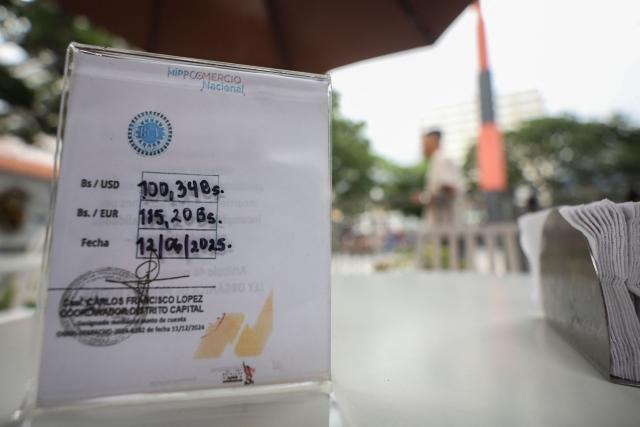 View of a sign showing the dollar rate of 100.33 Bolivars per 1 US Dollar, in Caracas, on June 12, 2025. The official exchange rate of the dollar surpassed the symbolic barrier of 100 bolivars, the local currency registering a devaluation of almost 50 per cent so far in 2025. At the end of the day, the dollar was trading at 101.08 bolivars according to the Central Bank, amid an offensive to curb the black market exchange. (Photo by Pedro MATTEY / AFP)