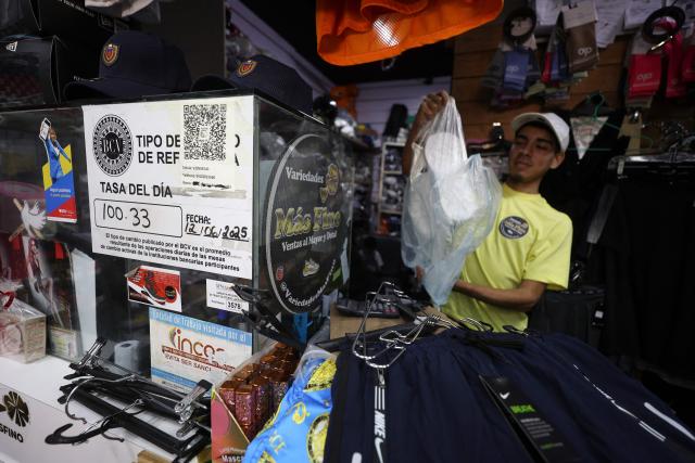 A worker accomodates goods next to a sign showing the dollar exchange rate in Caracas, on June 12, 2025. The official exchange rate of the dollar surpassed the symbolic barrier of 100 bolivars, the local currency registering a devaluation of almost 50 per cent so far in 2025. At the end of the day, the dollar was trading at 101.08 bolivars according to the Central Bank, amid an offensive to curb the black market exchange. (Photo by Pedro MATTEY / AFP)