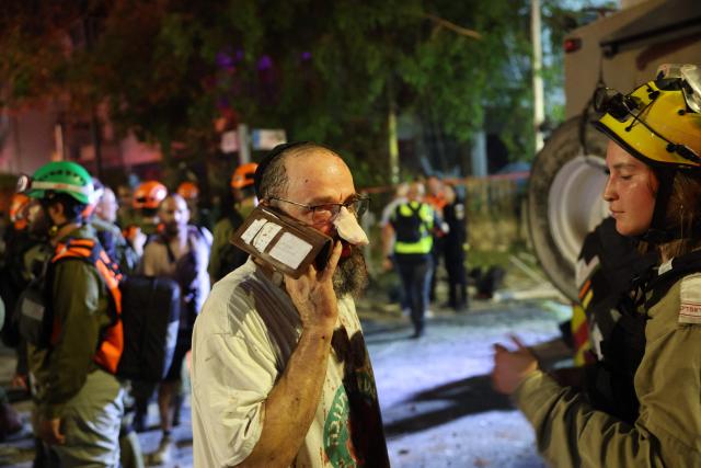 An injured man uses his telephone in an area hit by a missile fired from Iran, in Ramat Gan near Tel Aviv on June 13, 2025. Iran fired a barrage of ballistic missiles at Israel in a counter-strike in the evening on June 13, after an unprecedented onslaught hammered the Islamic republic's top military brass and targeted its nuclear facilities and bases. (Photo by Jack GUEZ / AFP)