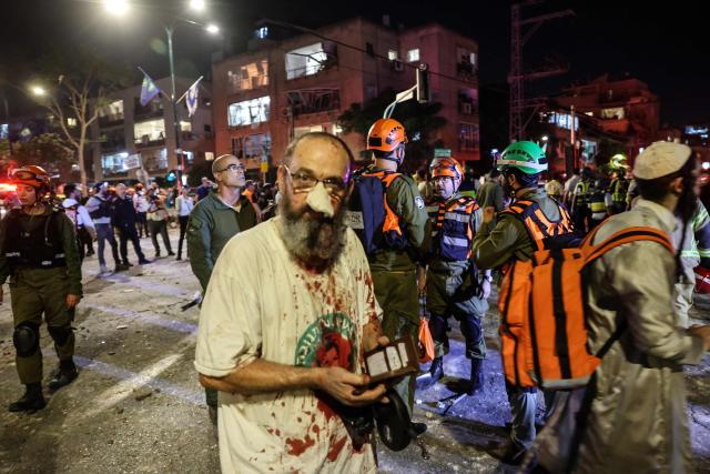 An injured man stands among first responders in an area hit by a missile fired from Iran, in Ramat Gan near Tel Aviv on June 13, 2025. Iran fired a barrage of ballistic missiles at Israel in a counter-strike in the evening on June 13, after an unprecedented onslaught hammered the Islamic republic's top military brass and targeted its nuclear facilities and bases. (Photo by Jack GUEZ / AFP)
