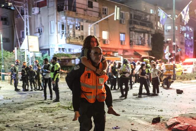 A rescuer carries an injured girl on his back in an area hit by a missile fired from Iran, in Ramat Gan near Tel Aviv on June 13, 2025. Iran fired a barrage of ballistic missiles at Israel in a counter-strike in the evening on June 13, after an unprecedented onslaught hammered the Islamic republic's top military brass and targeted its nuclear facilities and bases. (Photo by Jack GUEZ / AFP)